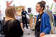 Zwei Frauen stehen in einem Veranstaltungsraum und unterhalten sich. Im Hintergrund sind weitere Personen zu sehen, die miteinander reden.