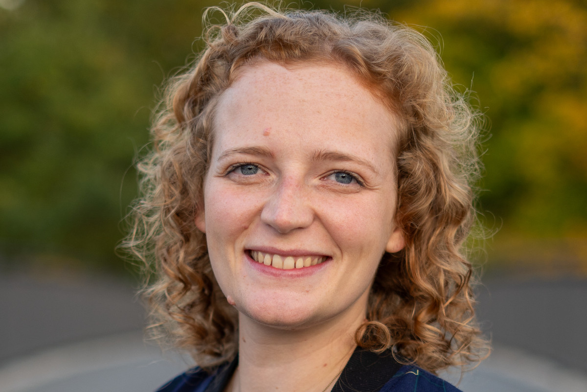 Eine Frau mit blonden, gelockten Haaren lacht freundlich in die Kamera.