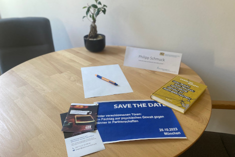 Auf einem Tisch liegen Flyer, ein Buch,Namenschild und Notizzettel mit Stift.