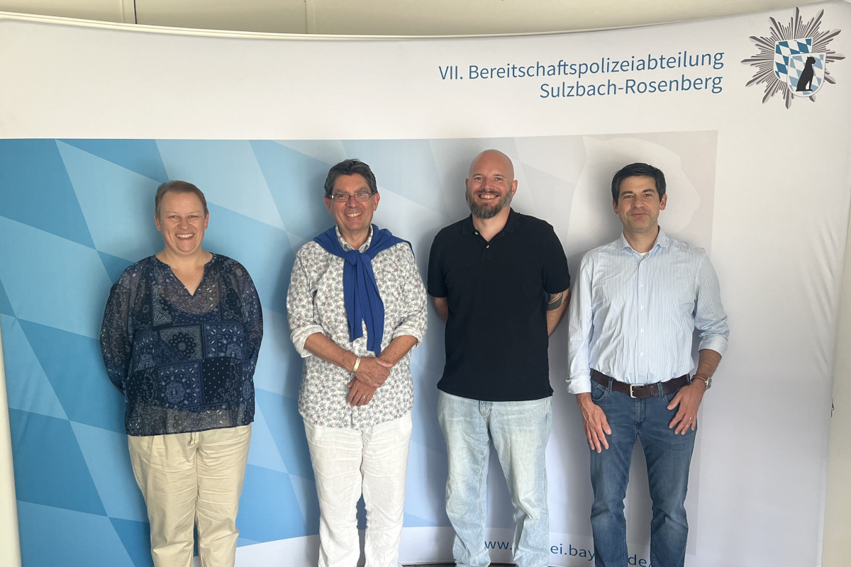 Die Allgemeinbildungslehrerin der Polizeischule steht mit den drei Referenten aus den Einrichtungen zum Thema Männergewaltschutz für ein Gruppenfoto vor einer Leinwand, auf der oben rechts das Logo der Polizeischule aufgedruckt ist.