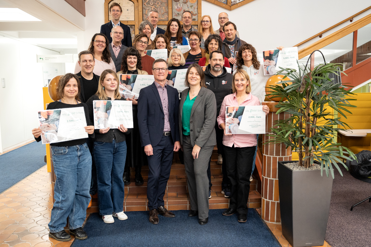Eine Gruppe von Menschen steht auf einer Treppe, einige halten Spendenurkunden hoch