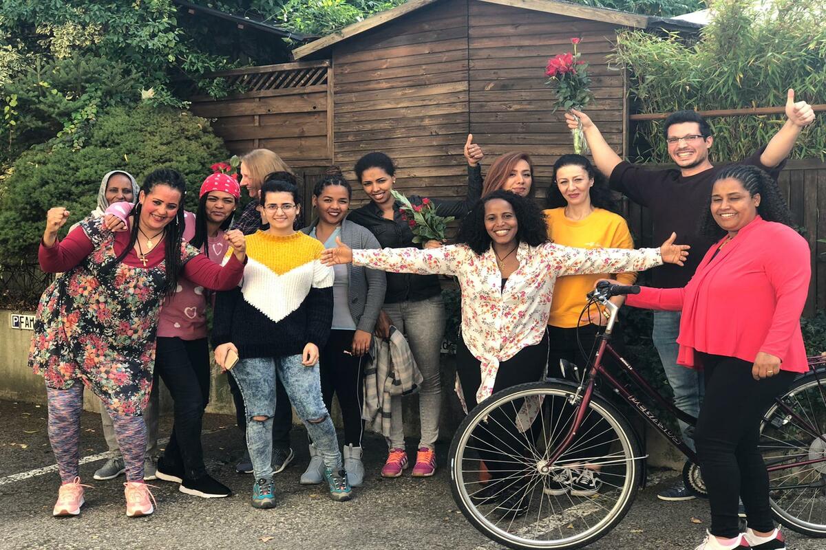 Viele Frauen und ein Mann stehen mit einem Fahrrad im Freien, sie halten Blumen in den Händen.