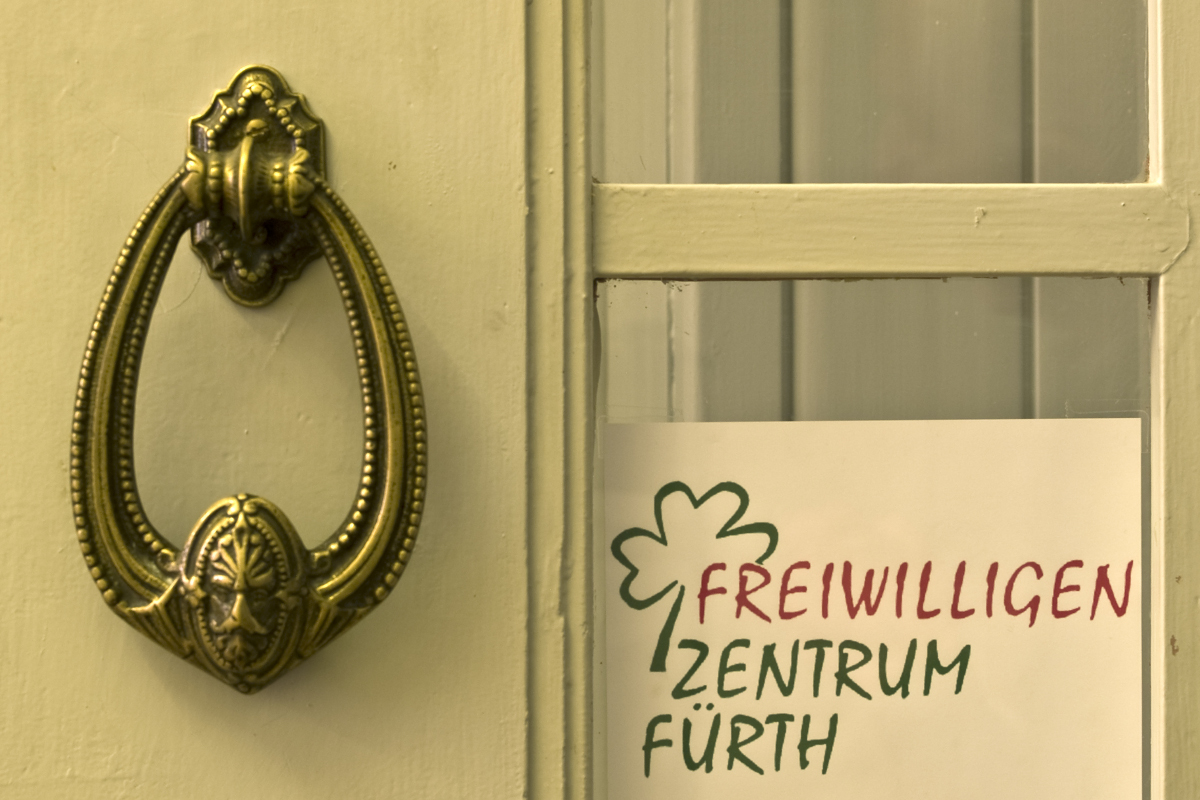 Nahaufnahme eines Türklopfers an einer Eingangstür, daneben hängt das Logo des Freiwilligenzentrums Fürth.