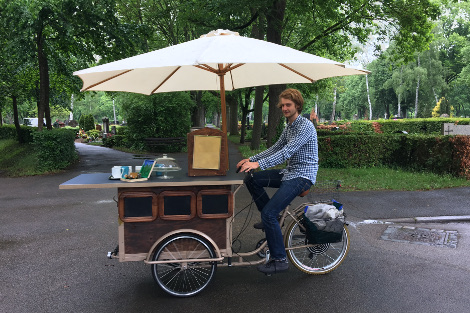 Ein Mitarbeiter fährt mit einem Lastenrad über den Friedhof