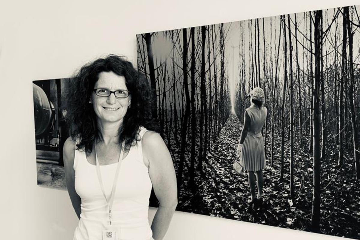 Porträt schwarz-weiß einer Frau mit weißem Trägerhemd und dunklen Locken, rechts neben ihr eine Fotografie von einer Frau im Wald.