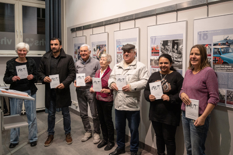 Sieben Personen stehen nebeneinander und halten ein Buch mit dem Titel MUT vor sich.