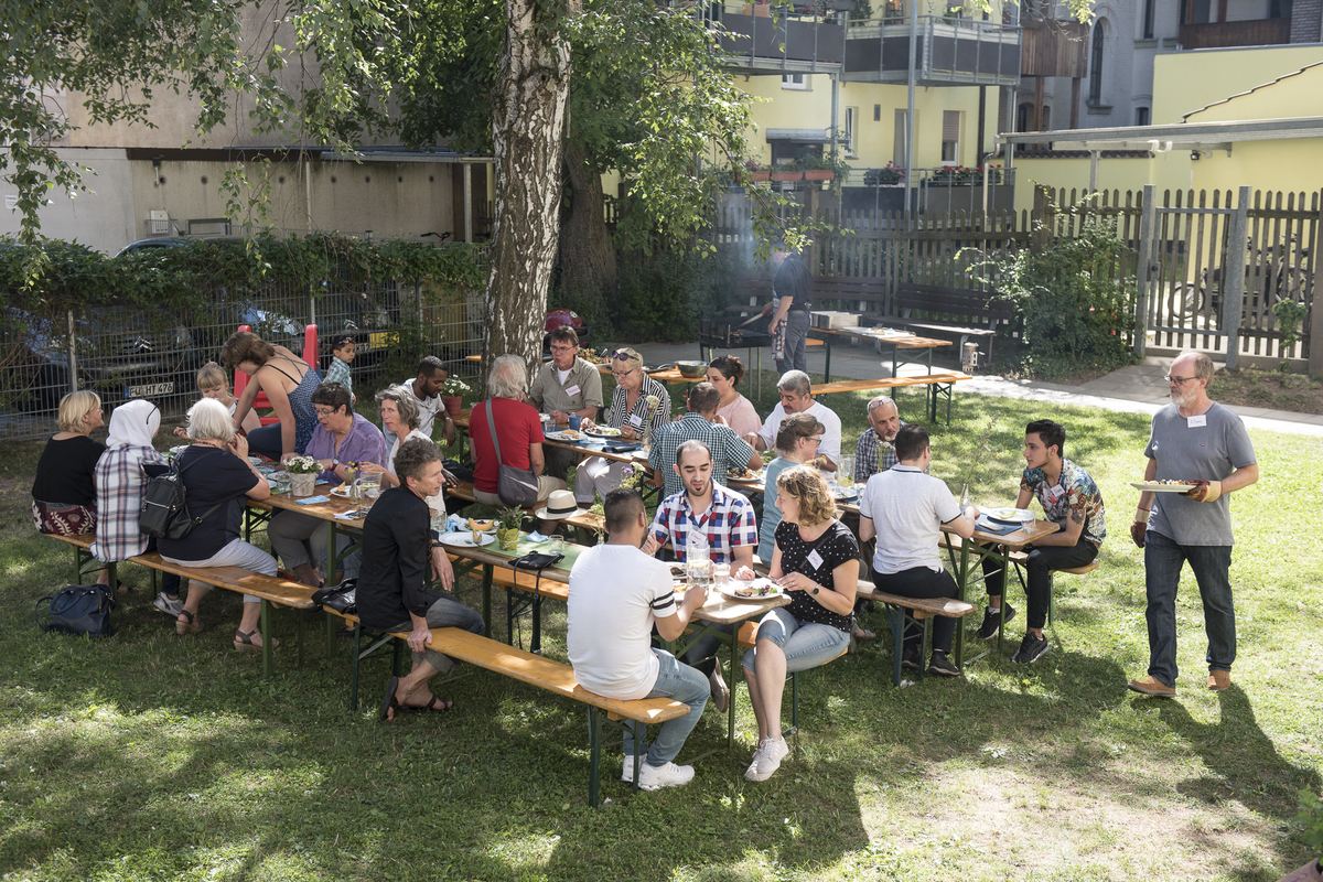 An Bierbankgarnituren sitzen viele Menschen und reden und essen miteinander