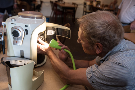 Ein Mann sitzt an einem Tisch und repariert eine Kaffeemaschine