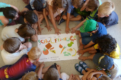 Kinder sitzen im Kreis um das Plakat vom gesunden Schulfrühstück