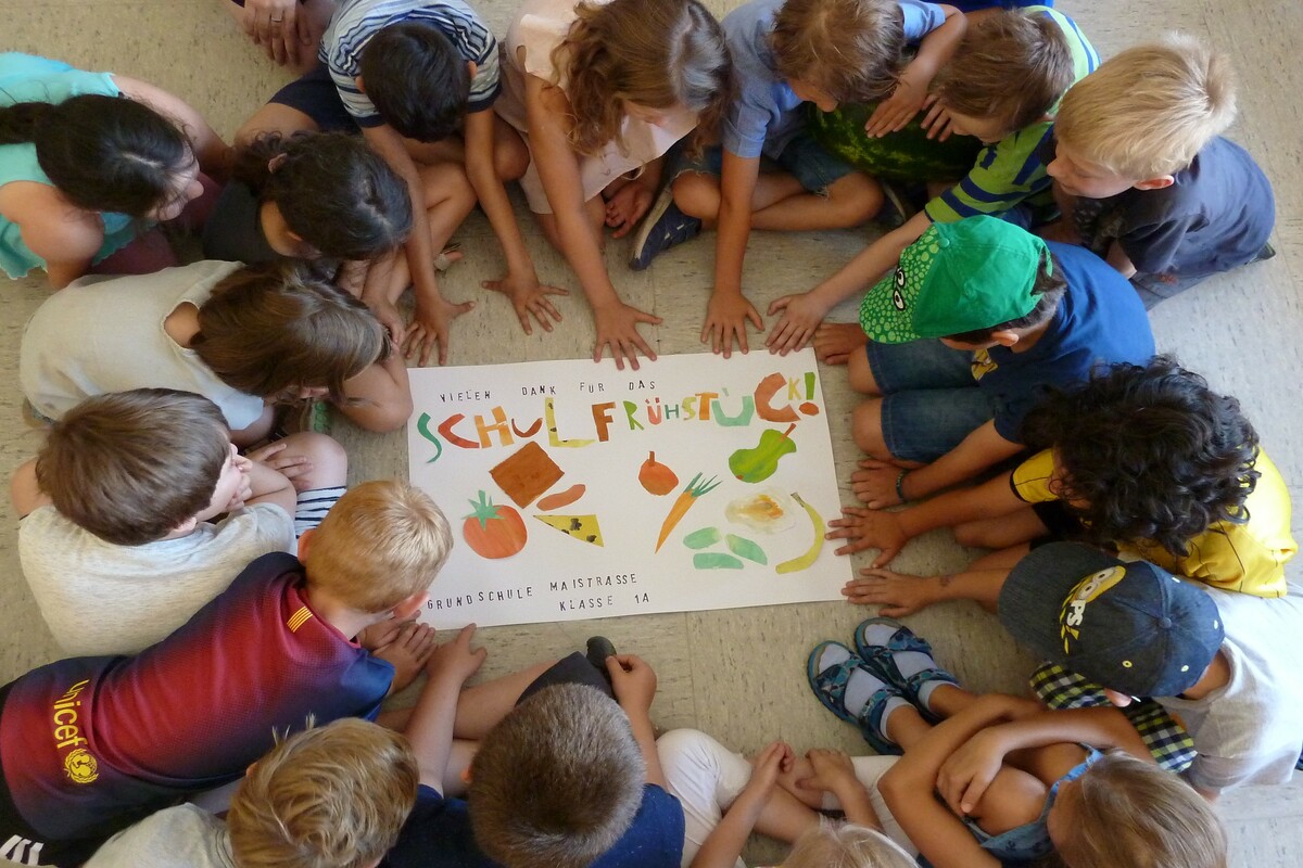 Kinder sitzen im Kreis um das Plakat vom gesunden Schulfrühstück