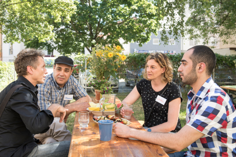 vier junge Menschen mit und ohne Migrationshintergrund sitzen draußen an einem Tisch und reden