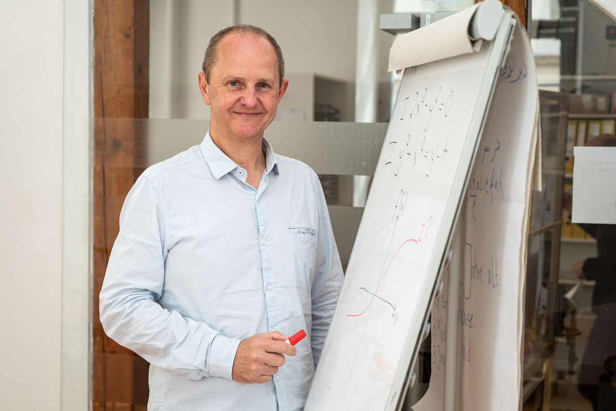 Ein Mann mit Stift in der Hand steht vor einer Flipchart und lächelt freundlich