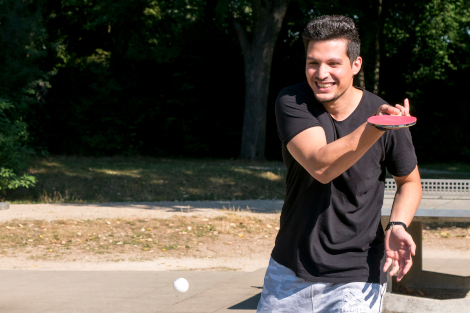 Ein junger Mann mit Tischtennisschläger in der Hand ist in Bewegung und lacht