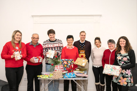 Einige Personen sind über einen Tisch voller Geschenke gebeugt und schauen sich die Päckchen an.