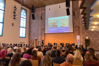 Ein Saal mit vielen Menschen, die einer Referentin zuhören.