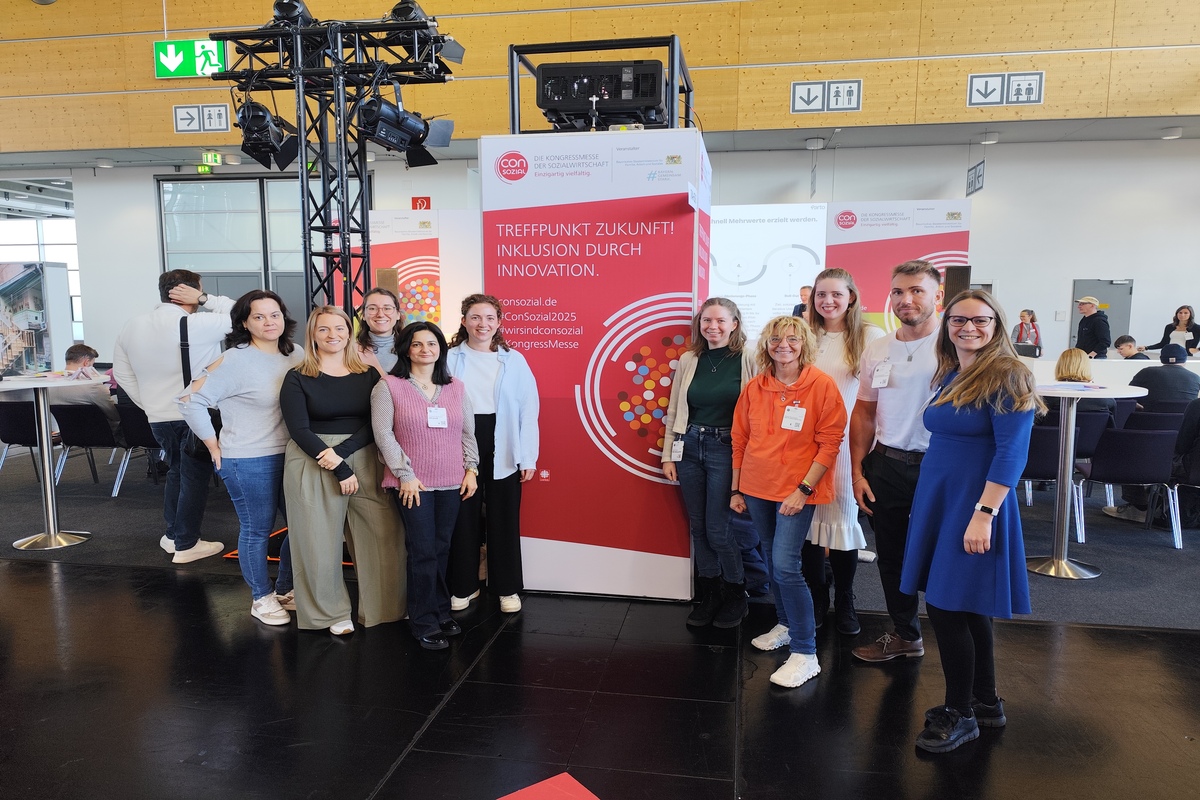 Auf dem Bild stehen Mitarbeitende der Fachdienste Bildungschancen und ISAK zusammen mit Kolleginnen der Kita MOMO vor einem großen ConSozial-Logo.