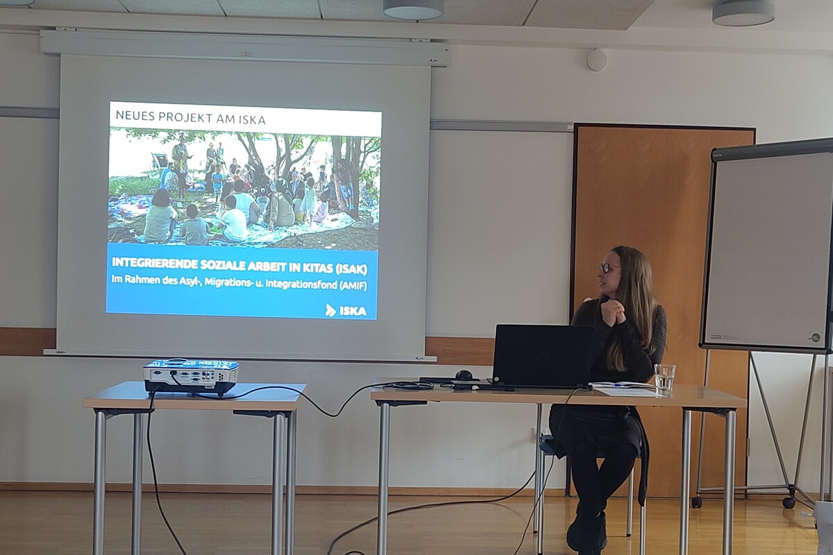 Eine Frau sitzt vor einer Leinwand, auf die eine Präsentation projiziert wird, und blickt auf diese.