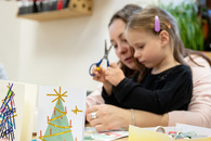 Ein Mädchen sitzt bei ihrer Mutter auf dem Schoß, während sie gemeinsam etwas basteln.