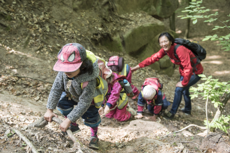Mutter hilft vier Kindern im Wald einen steilen Hügel zu besteigen
