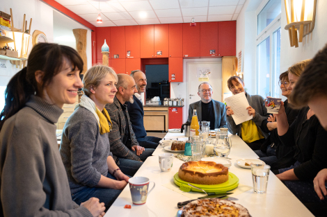 Um einem Tisch mit Kaffee und Kuchen sitzen mehrere Personen, lachend und redend.