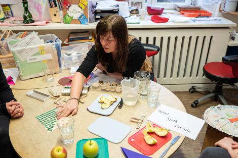 Eine Frau ist über einem Tisch über unterschiedliche Materialien gebeugt.
