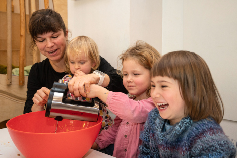 Eine Frau und drei Kinder mixen zusammen in einer großen, roten Rührschüssel.