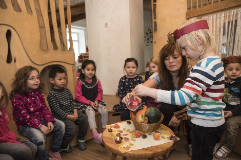 Kinder sitzen im Kreis, Erzieherin zündet mit Kind Kerze an