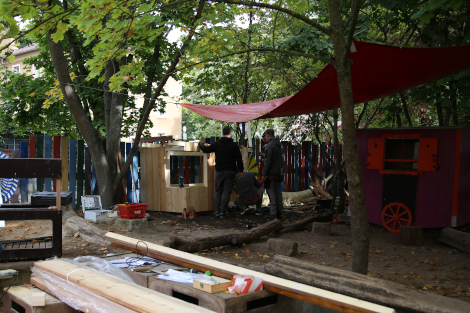 In einem Hof mit vielen Spielutensilien sieht man mehrere Männer an einer Hütte bauen