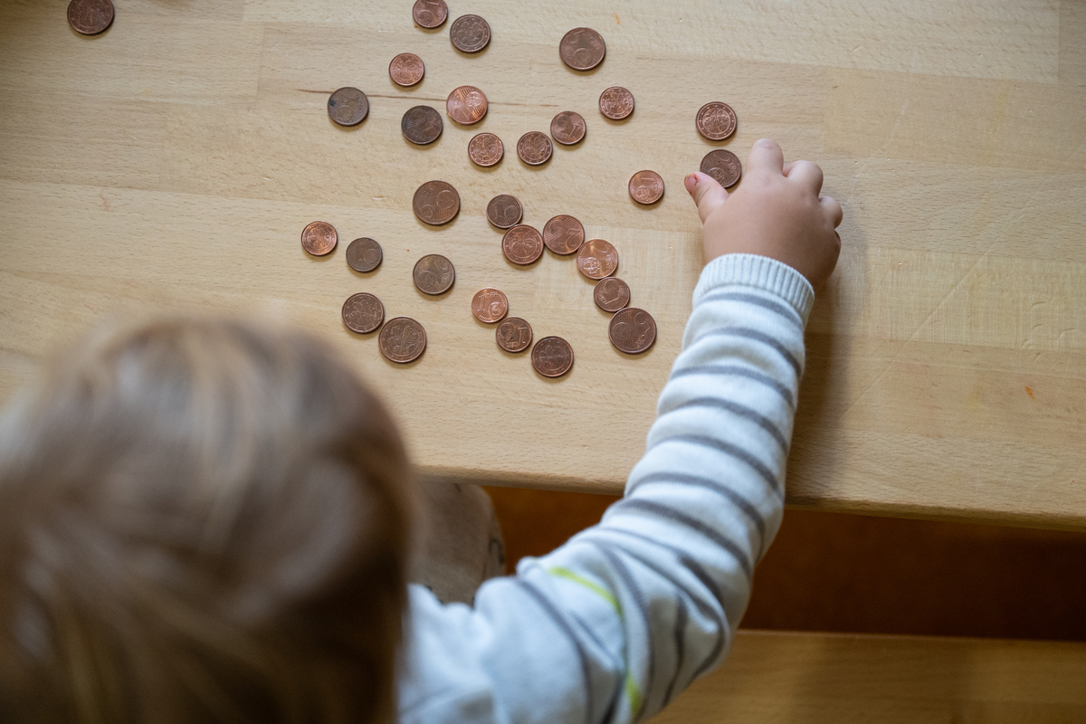 Centstücke liegen auf einem Tisch. Ein Kind mit braunen Haaren spielt mit ihnen.