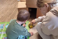 Eine junge Praktikantin und ein Kind spielen mit einer elektronischen Biene. Sie sind von hinten zu sehen.