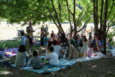 Auf einer Decke im Park unter einem großen Baum sitzen einige Kinder und Erwachsene