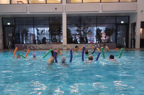 Im Schwimmbad sind eine Gruppe Kinder mit bunten Schwimmnudeln im Becken