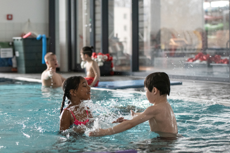 Zwei Kinder plantschen lachend im Schwimmbecken.