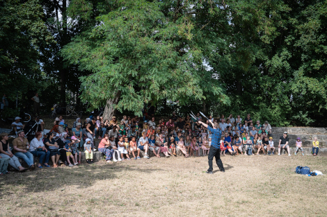 Ein Mann jongliert vor Publikum, welches im Halbkreis vor ihm sitzt.