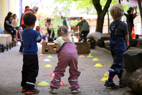 Drei Kinder stehen mit dem Rücken zur Kamera und konzentrieren sich auf ein Ballspiel