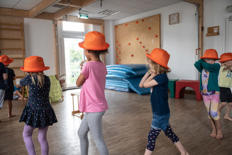 Kinder mit roten Hütenauf dem Kopf laufen im Raum im Kreis.