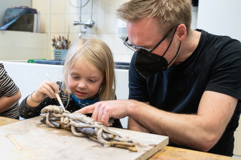 Ein kleines Mädchen formt gemeinsam mit ihrem Vater konzentriert ein Gebilde aus Ton