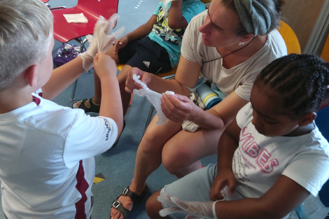 Zwei Kinder und eine Frau ziehen sich Plastikhandschuhe über