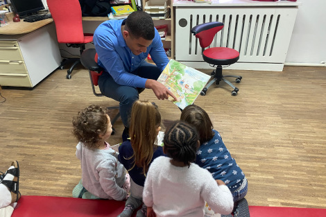 Ein Mann sitzt mit vier Kindern zusammen und liest ihnen ein Bilderbuch vor.