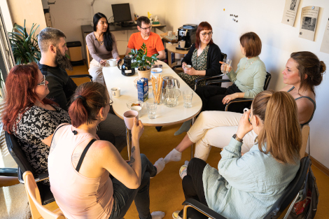 Neun Personen sitzen um einen Tisch, unterhalten sich und trinken Kafee.