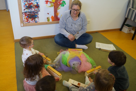 Eine Pädagogin und fünf Kinder sitzen mitKlanginstrumenten am Boden