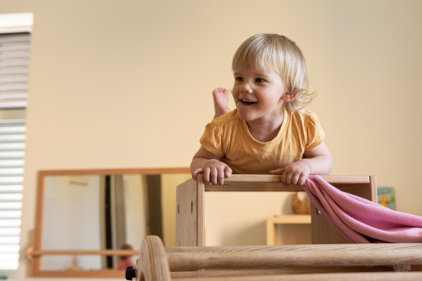 Ein Kleinkind liegt stolz auf einem Holzelement, auf das es geklettert ist.