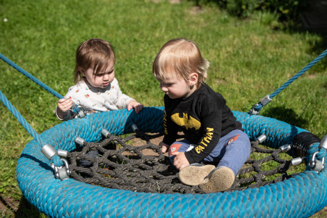 Zwei Kleinkinder spielen draußen an einer Schaukel