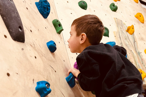 Nahaufnahme von einem Jungen, der sich an einer Bouldernwand festhält.