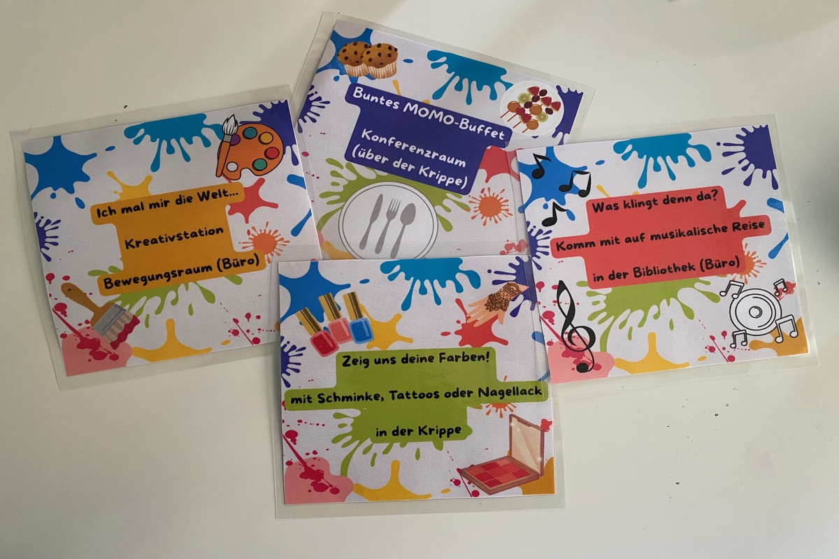 Das Bild zeigt mehrere bunt gestaltete Schilder, die die Stationen des Familienfests markieren, darunter Kreativstation, Buffet, Musikangebot und Schminkstation.