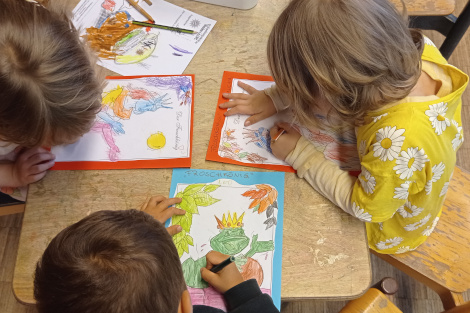 Drei Kinder sitzen um einen Tisch und malen Froschkönig-Bilder aus