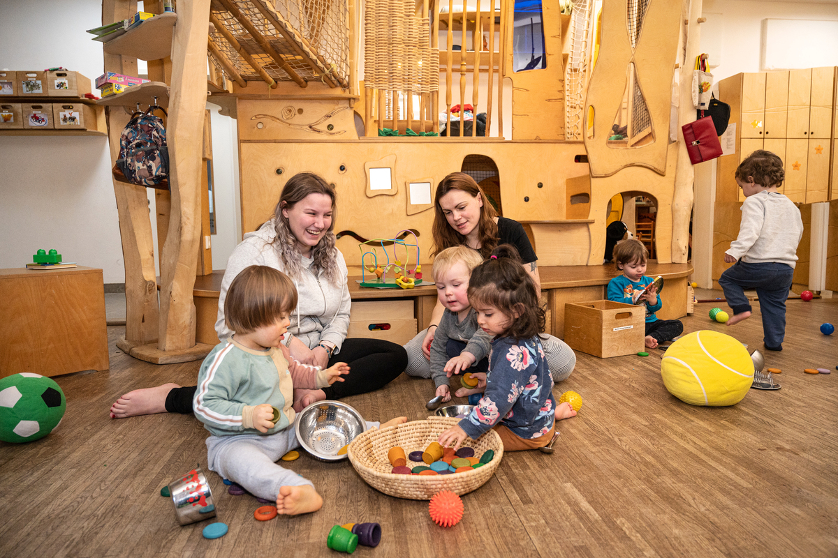 Zwei junge Frauen sitzen mit drei Kindern auf dem Boden und spielen.