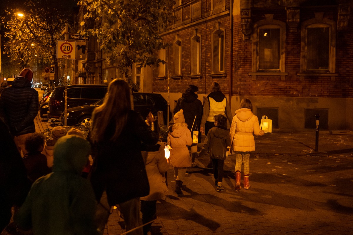 Mehrere Familien laufen im Dunkeln über eine Straße, die Kinder haben Laternen in der Hand.