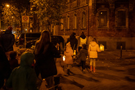 Mehrere Familien laufen im Dunkeln &uuml;ber eine Stra&szlig;e, die Kinder haben Laternen in der Hand.