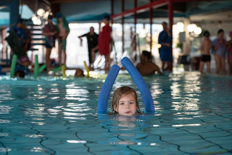 Ein Mädchen mit Schwimmnudel streckt den Kopf aus dem Wasser